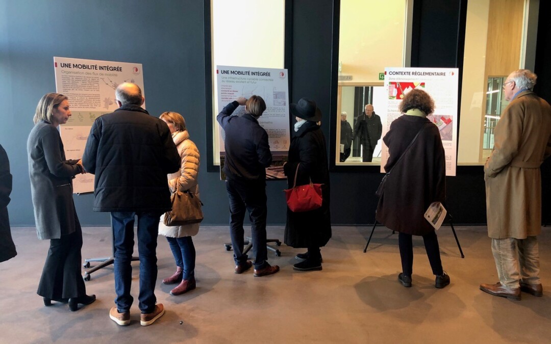 Visiteurs consultant des panneaux d'exposition intitulés « Une mobilité intégrée » et « Contexte réglementaire » dans un couloir aux murs sombres.