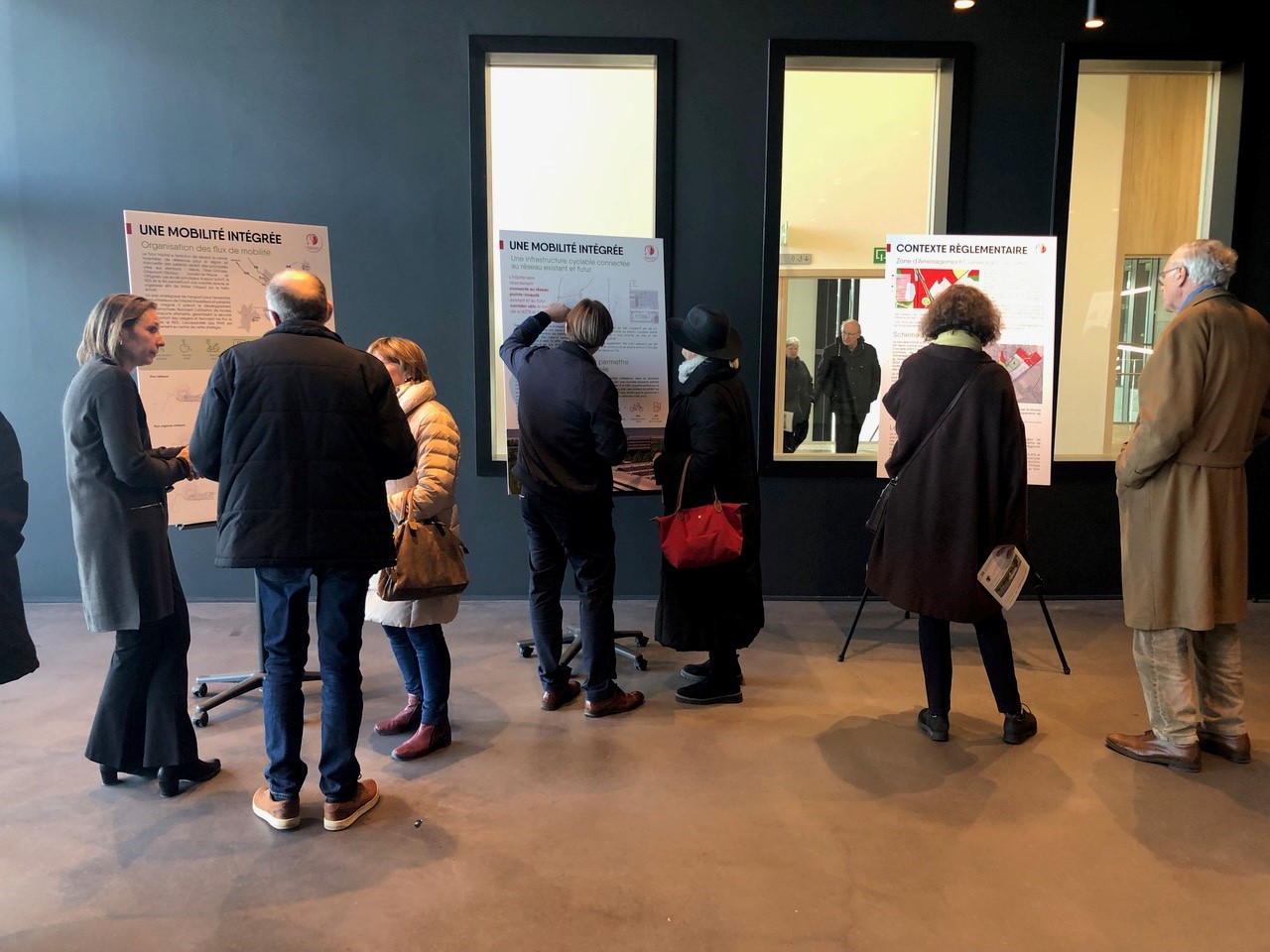 Gestion durable des eaux_Naturem Visiteurs consultant des panneaux d'exposition intitulés « Une mobilité intégrée » et « Contexte réglementaire » dans un couloir aux murs sombres.