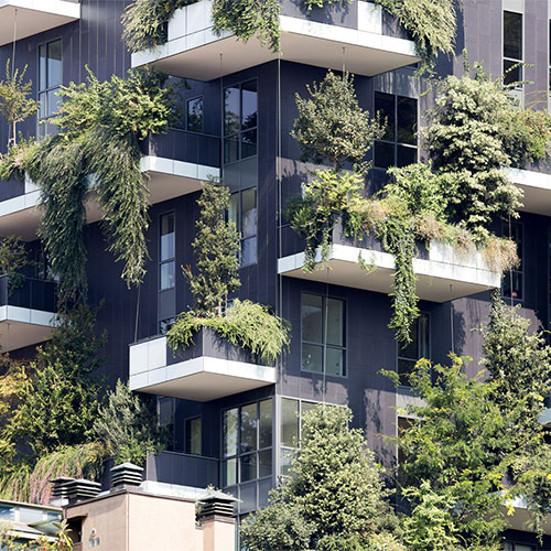 Façade d'immeuble moderne aux larges balcons débordant de végétation luxuriante et de plantes grimpantes, illustrant l'intégration de la nature dans l'architecture urbaine.